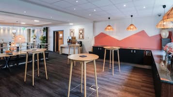 A modern hotel lobby with wooden tables, a reception desk, and a wall with abstract art.