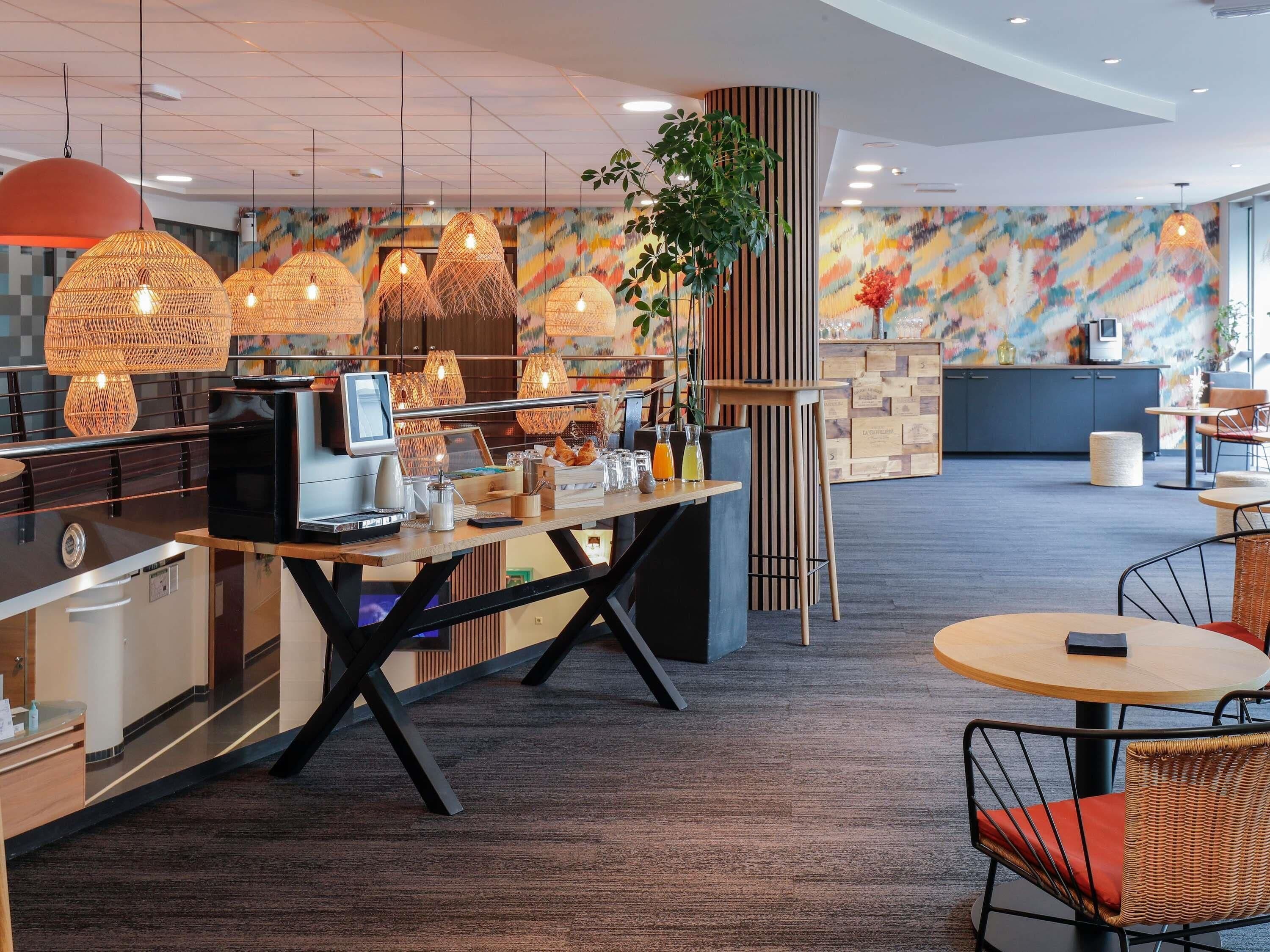 Un café moderne avec un comptoir en bois, des chaises en osier et des lampes en rotin suspendues au plafond.