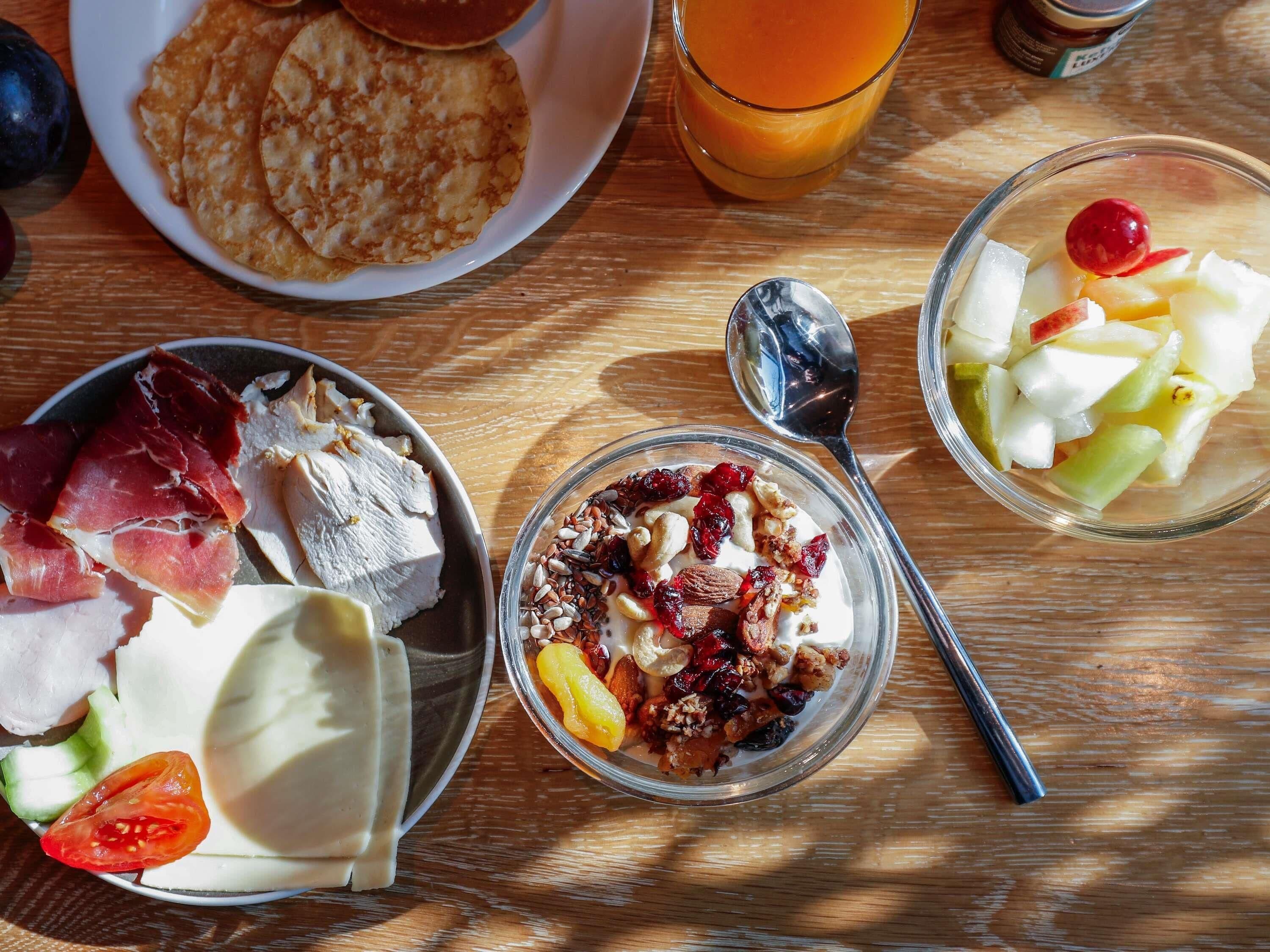 A breakfast table with various food items including pancakes, fruit, yogurt, and cheese.