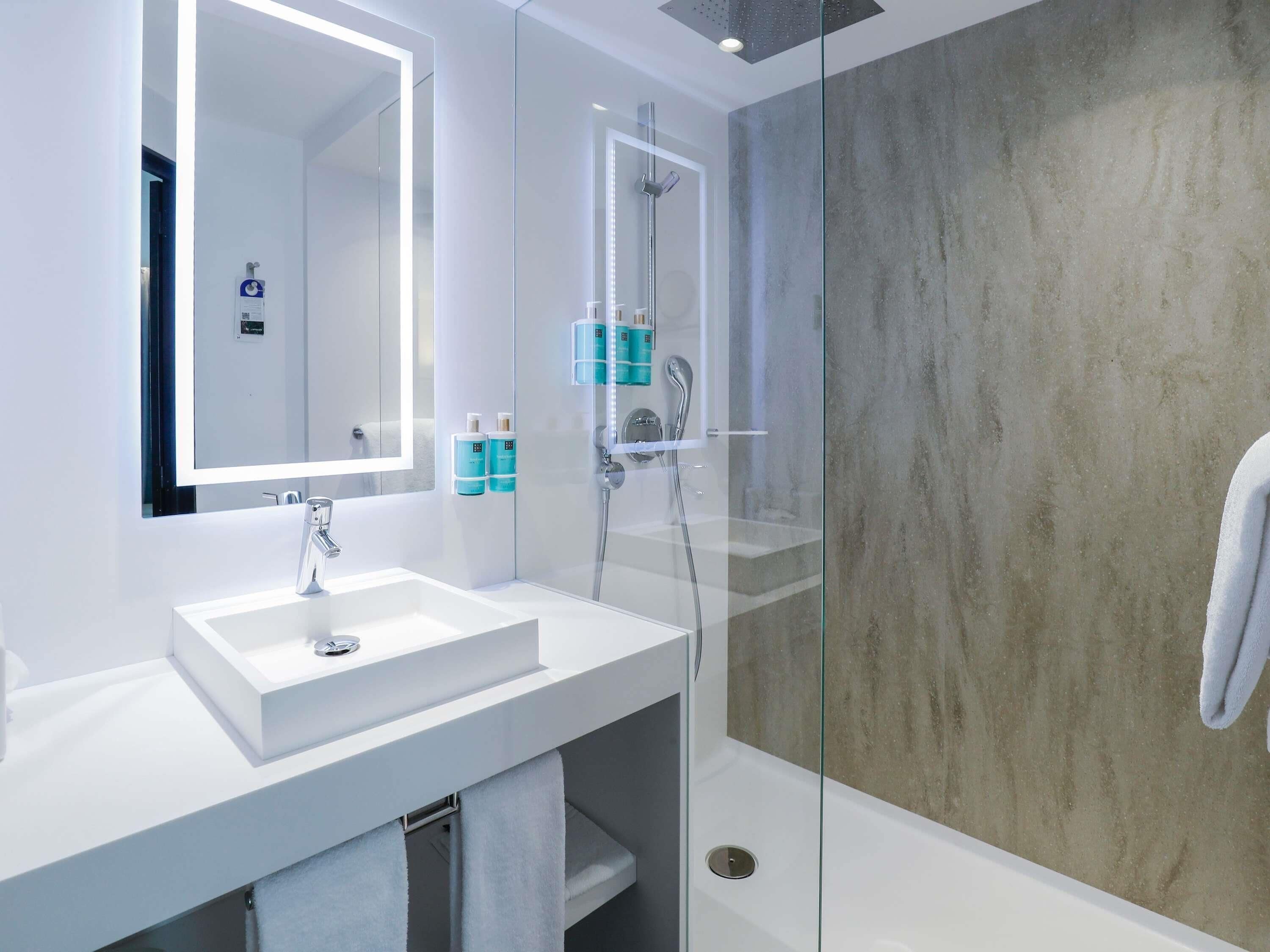 A modern bathroom with a white sink, a large mirror, and a glass-enclosed shower area.
