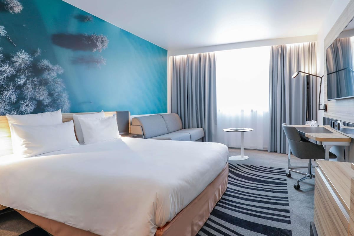 A hotel room with a large bed, a desk, a chair, and a TV.