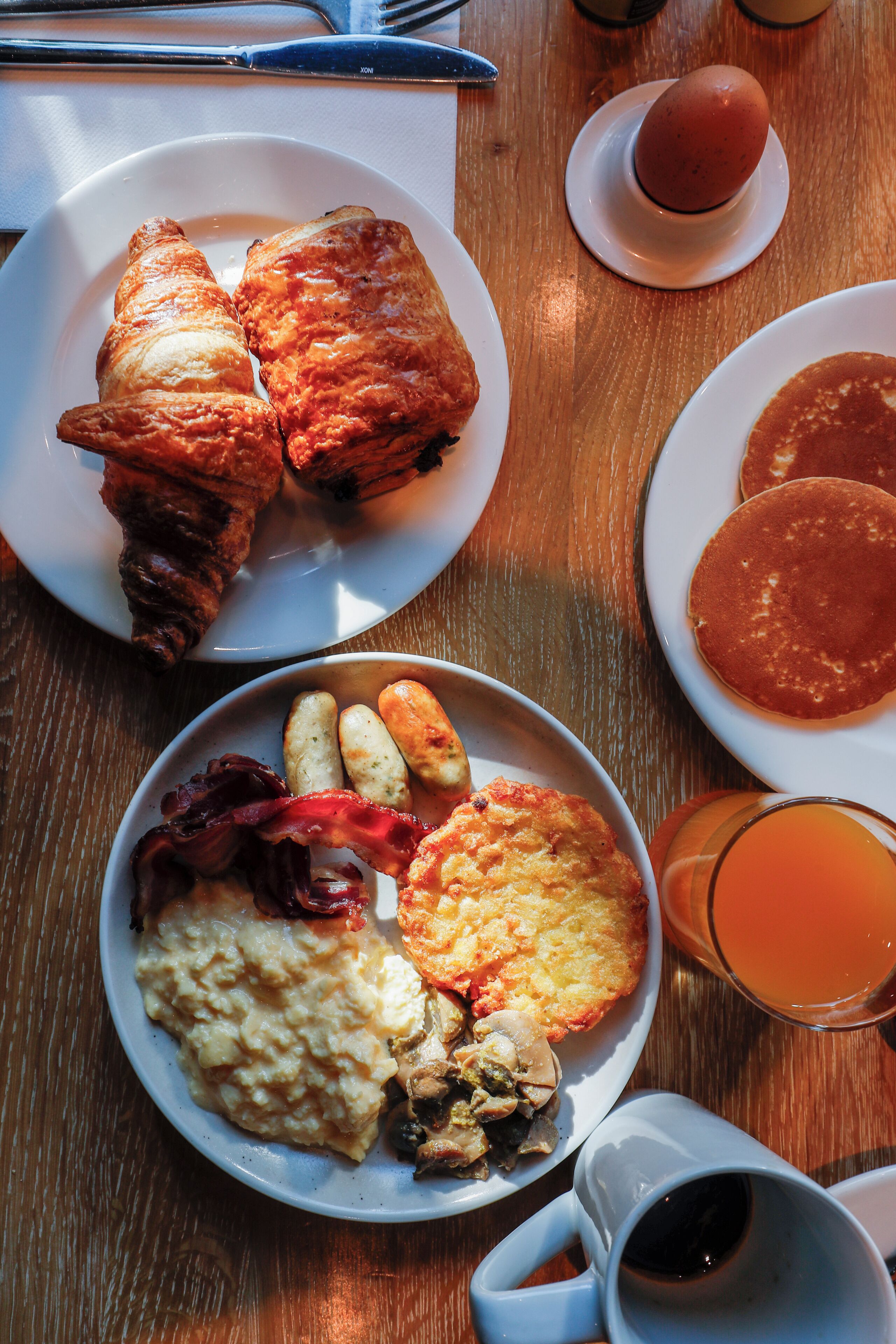 Une table mise pour le petit-déjeuner, avec des assiettes remplies de nourriture, une tasse de thé et un verre de jus d’orange.