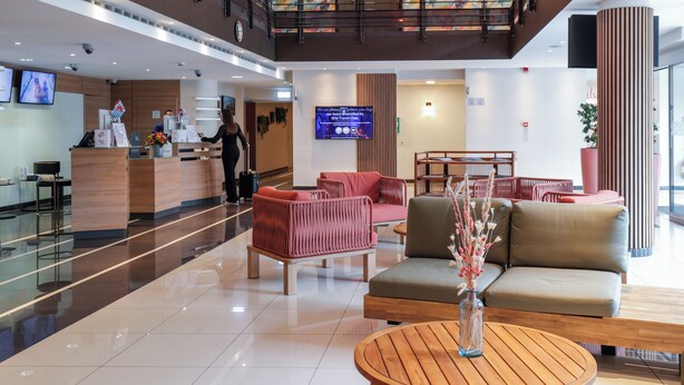 A modern hotel lobby with a reception desk, seating area, and a digital display.