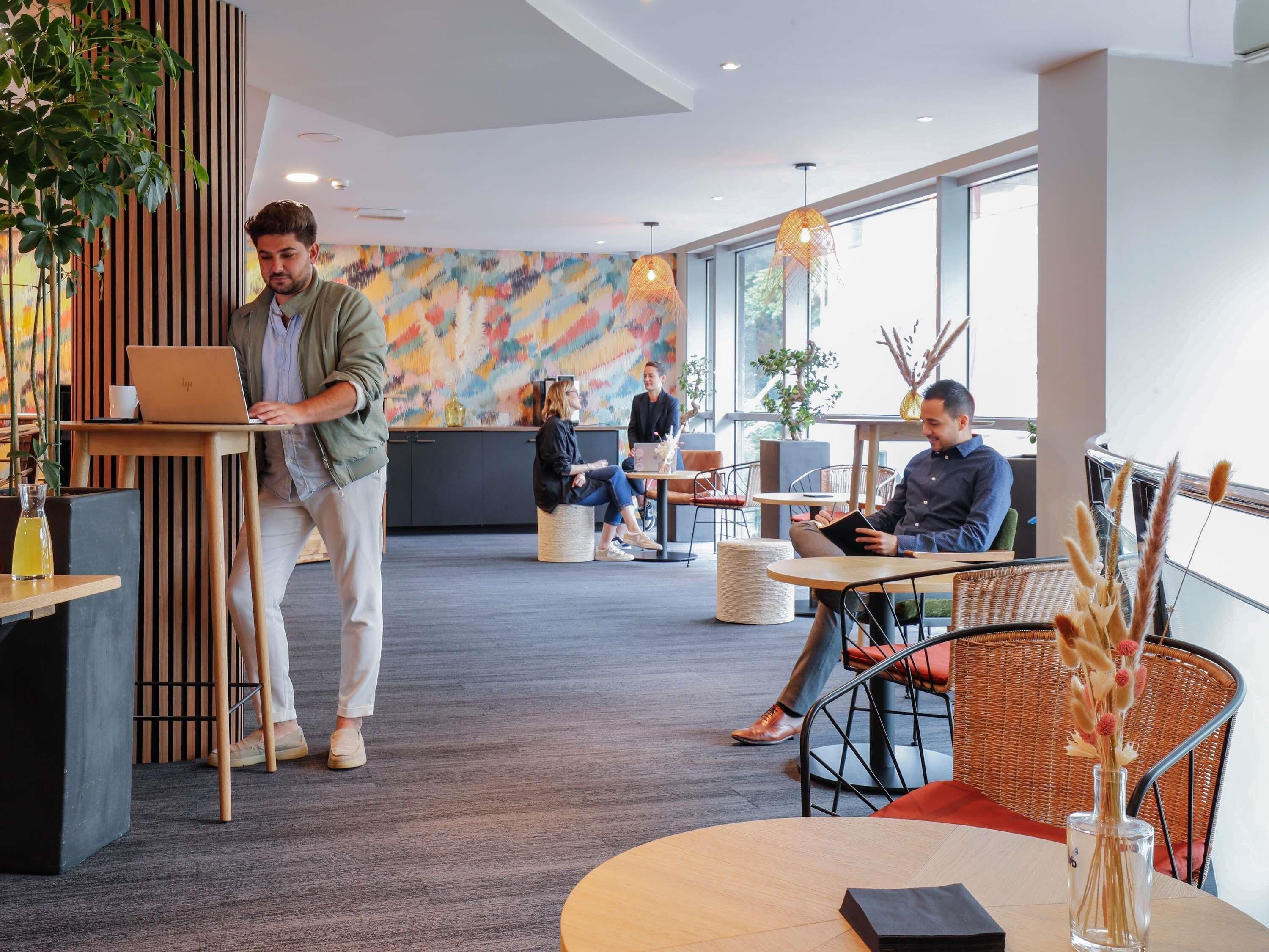 A modern cafe with wooden accents, large windows, and a colorful abstract wall.