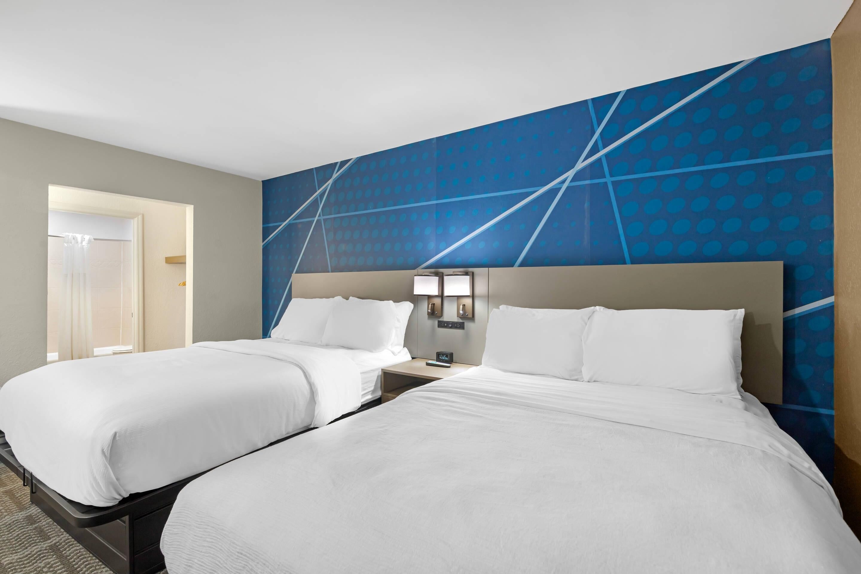 Ein Hotelzimmer mit zwei Betten, einem Nachttisch, einer Wandlampe und einer Tür zu einem Badezimmer.