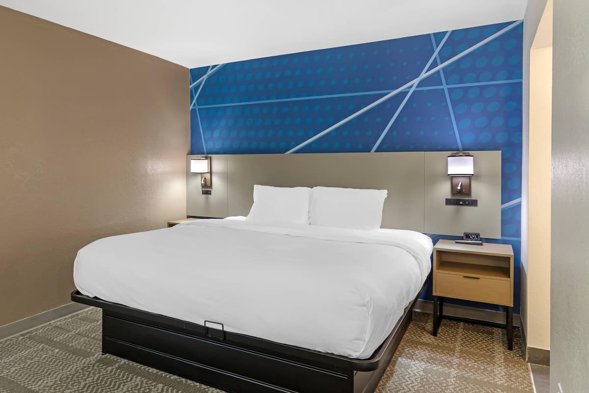 A hotel room with a bed, nightstands, a wall clock, and a patterned wall.