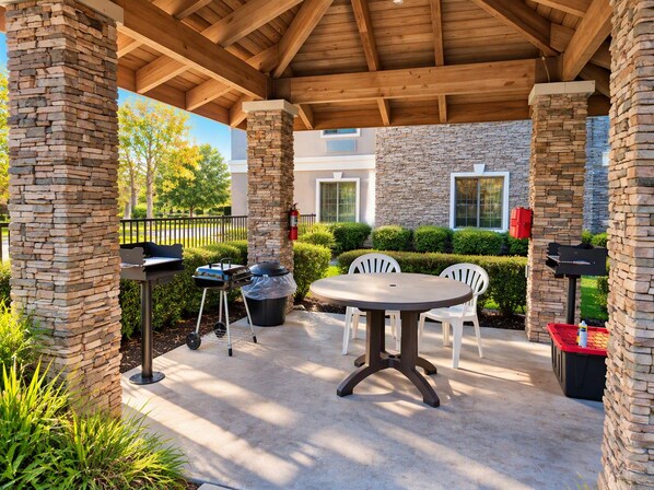 An outdoor patio with stone pillars, a grill, a table, and chairs.