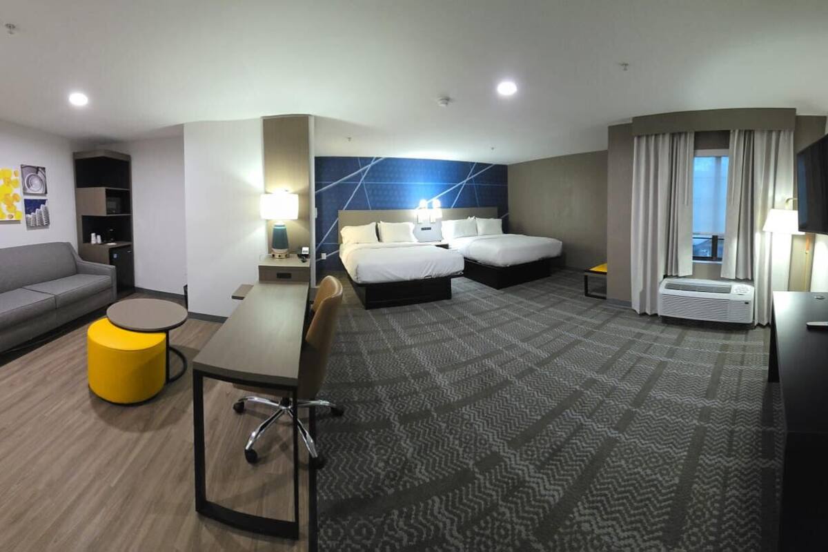 A hotel room with a bed, a sofa, a desk, a TV, and a window with curtains.