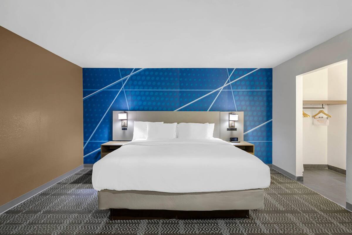 A hotel room with a large bed, two bedside tables with lamps, a blue patterned wall, and a wardrobe.
