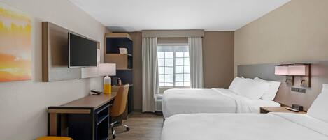Una habitación de hotel con dos camas, un escritorio, una silla, un televisor y una ventana con cortinas.