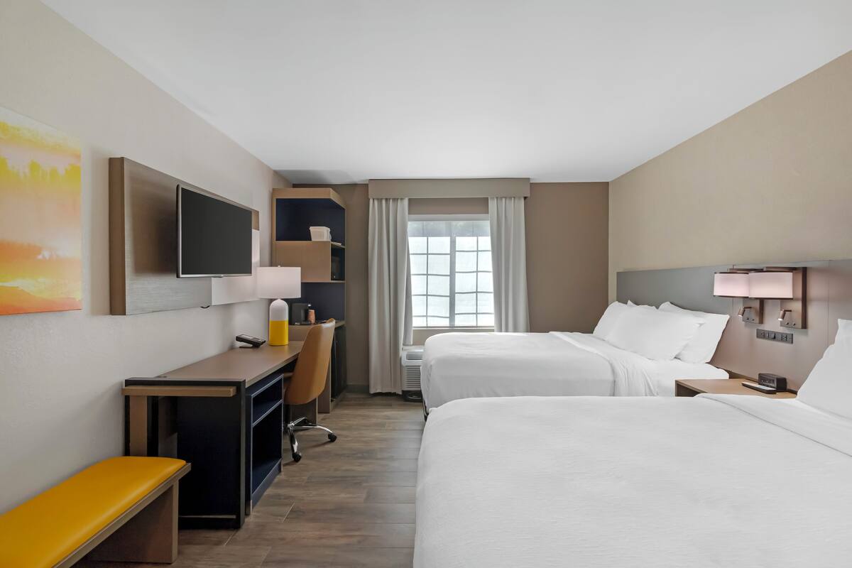 A hotel room with two beds, a desk, a chair, a TV, and a window with curtains.