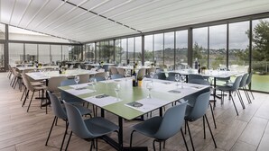 A spacious dining area with multiple tables and chairs, large windows offering a view of the landscape, and a modern ceiling design.
