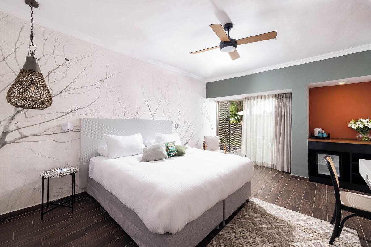Un dormitorio moderno con una cama grande, ventilador de techo, lámpara colgante y vistas al exterior por una puerta corrediza.