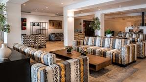 A spacious living area with patterned sofas and a coffee table, featuring a large painting and a potted plant.