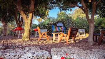 Un área de estar al aire libre con sillas y mesa de madera, rodeada de árboles y rocas.