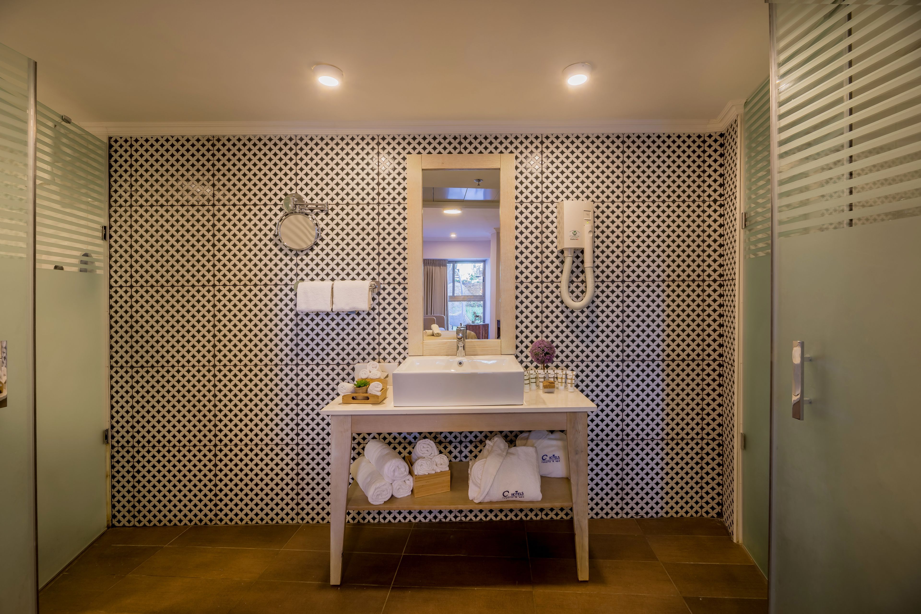 A bathroom with a patterned wall, a sink with a mirror, a towel rack, and a shower area.