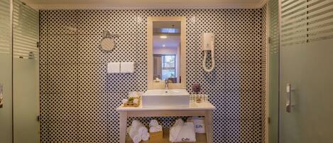 A bathroom with a patterned wall, a sink with a mirror, a towel rack, and a shower area.