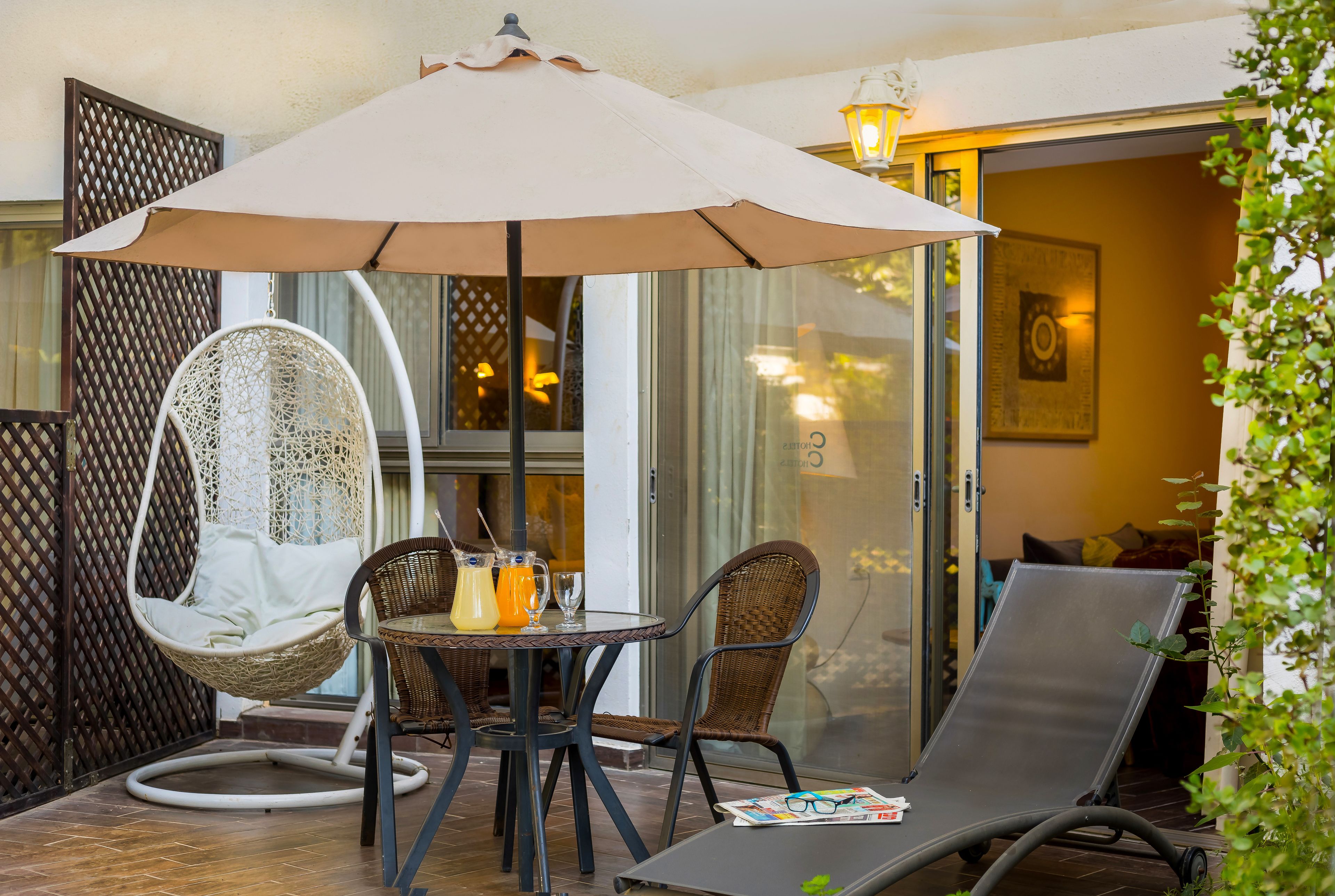 Un patio con una silla colgante, una mesa con bebidas y un sillón de descanso.