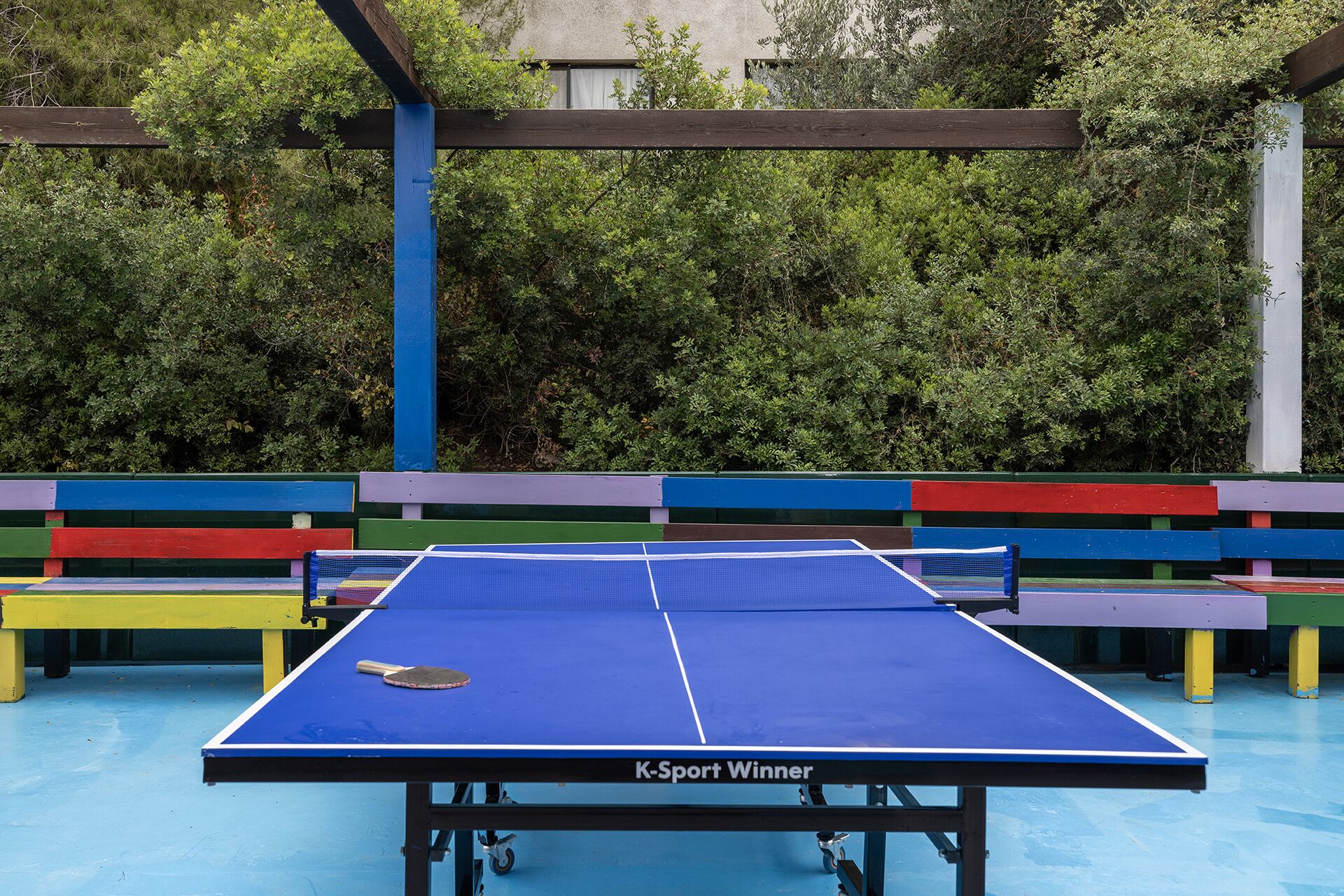 Une table de ping-pong avec un plateau bleu et un filet, entourée de bancs aux couleurs vives.
