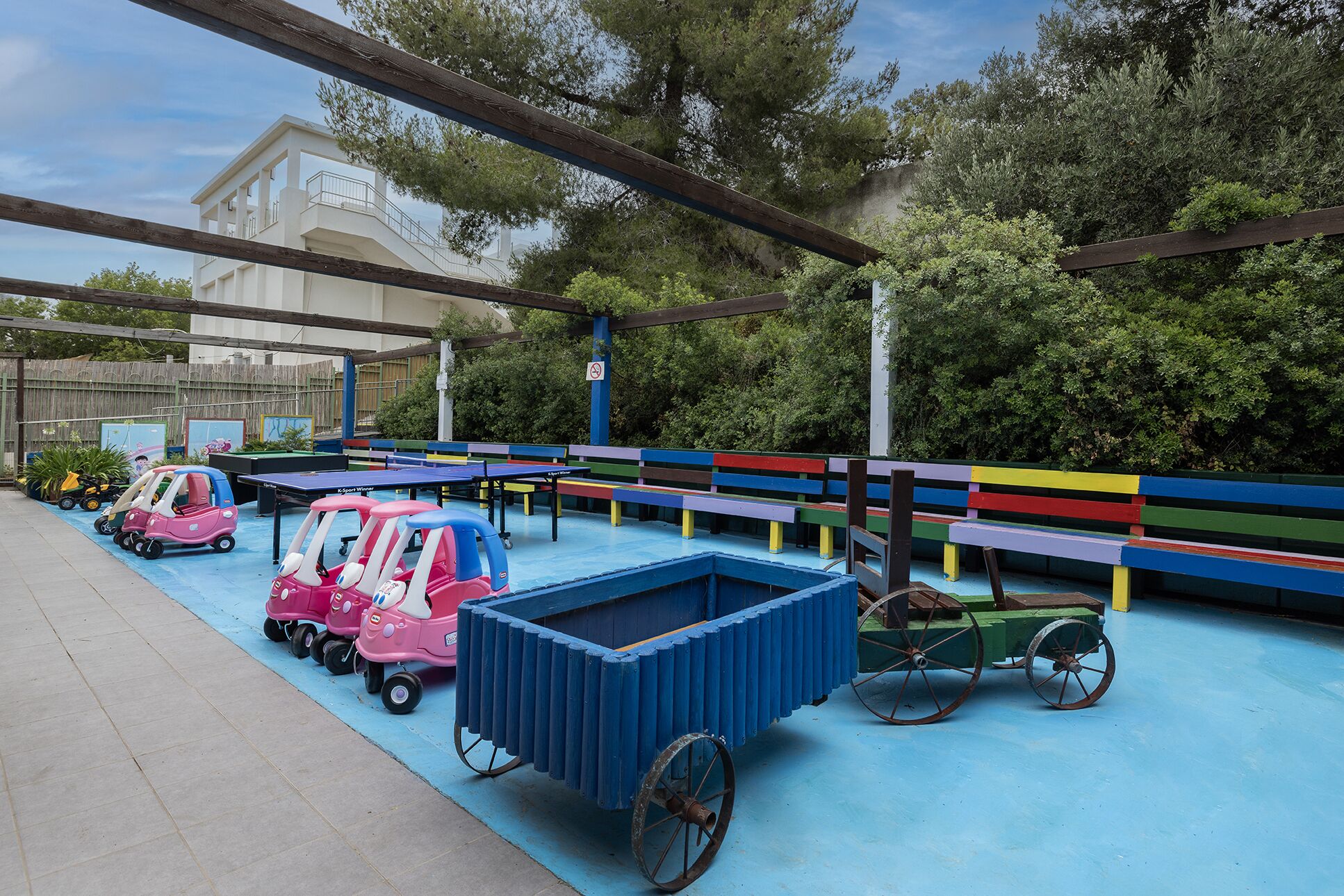 Zona de juegos infantiles con piso azul, bancos coloridos y coches de juguete.