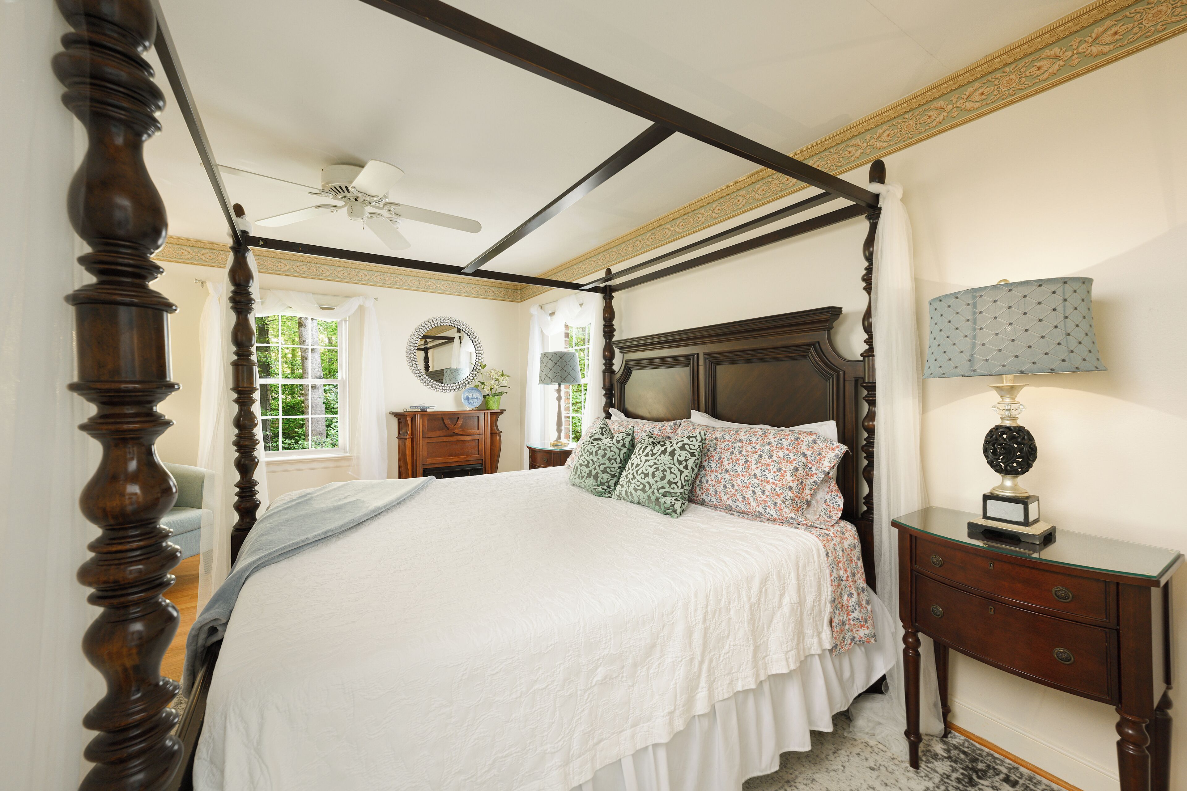A four-poster bed with a wooden headboard, a bedside table with a lamp, and a mirror on the wall.