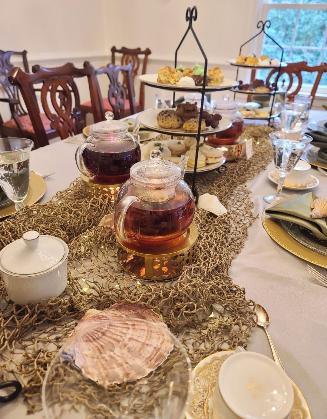 Una mesa dispuesta para una comida, con servicio de té, varios pasteles y un centro de mesa decorativo.