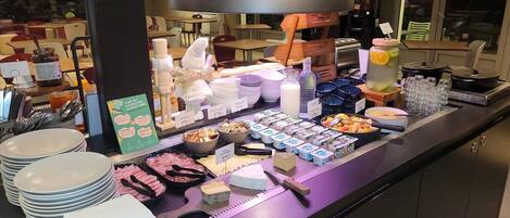 A buffet counter with various food items and beverages, including plates, bowls, and containers of yogurt and cheese.