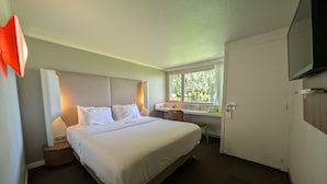 Une chambre d’hôtel comprenant un lit, des tables de chevet, un bureau avec une chaise, une fenêtre donnant sur un paysage agréable et un téléviseur.