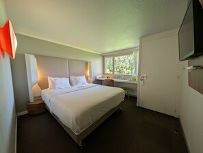 Habitación de hotel con cama, mesitas de noche, escritorio con silla, ventana con vista y televisión.