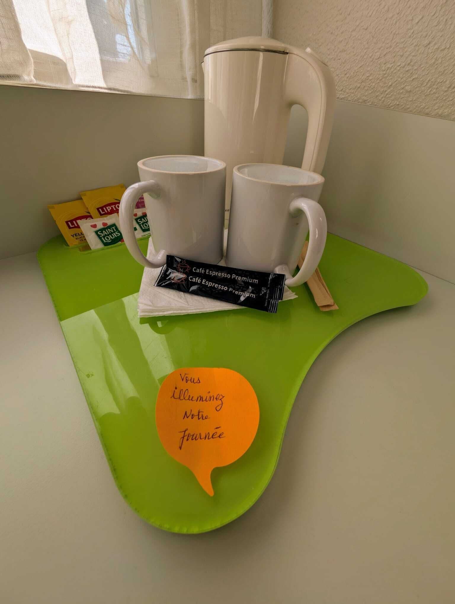 Una bandeja verde con dos tazas blancas, un paquete de café y una nota en el alféizar de una ventana.