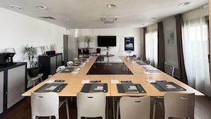 Une salle de conférence avec une longue table, des chaises, des étiquettes nominatives et un écran de télévision.