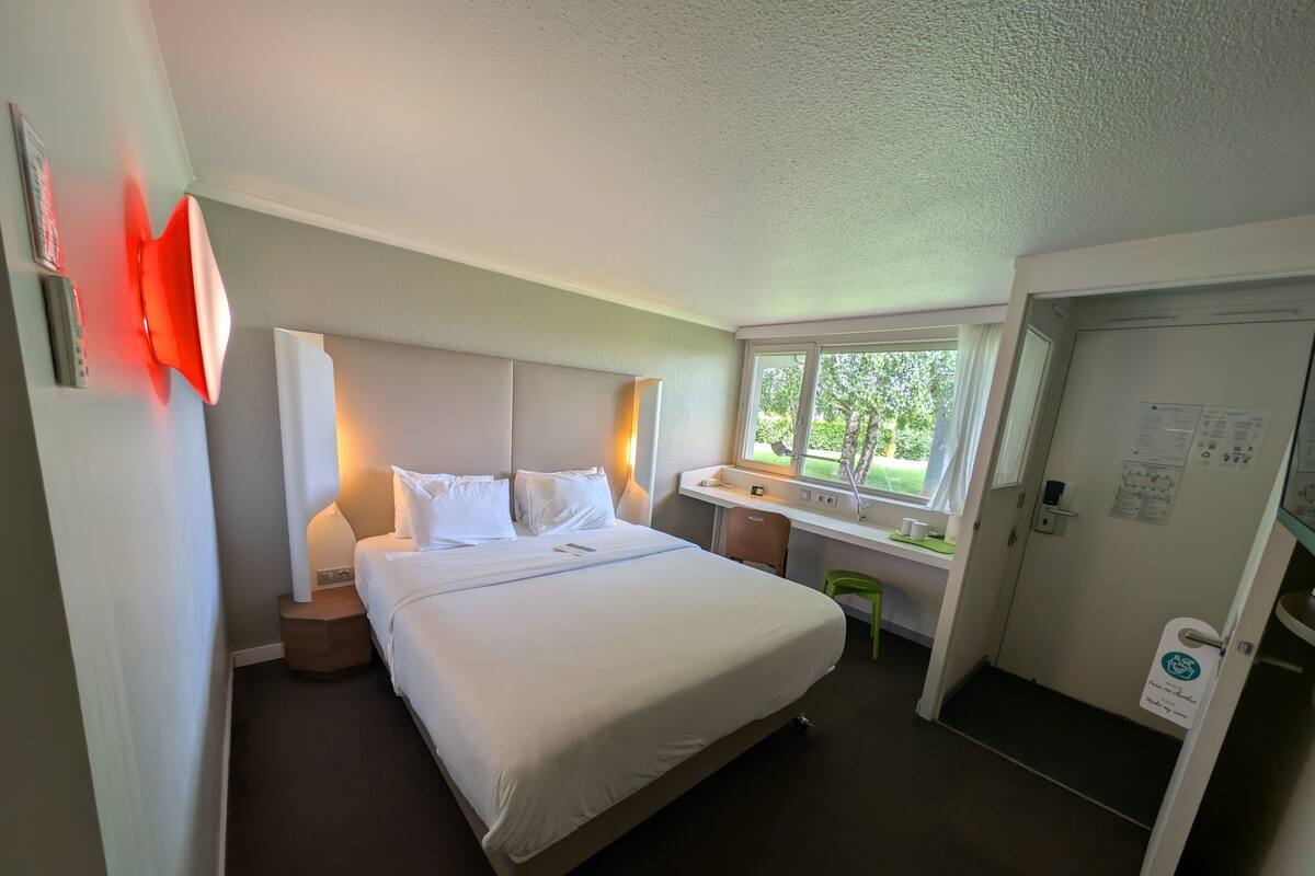 Ein Hotelzimmer mit Bett, Nachttisch, Fenster und einer Tür mit einem Schild.