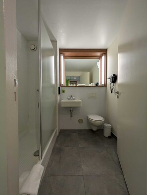 A compact bathroom with a shower, toilet, sink, and a hairdryer mounted on the wall. - Campanile Villejust - ZA Courtaboeuf (Villejust)