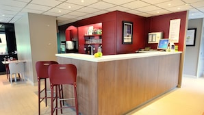 Un espace bar moderne avec un comptoir en bois, des tabourets de bar rouges et un écran numérique.