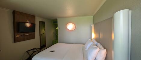 Una habitación de hotel con una cama, un televisor instalado en la pared, una mesita de noche y una lámpara fijada a la pared.