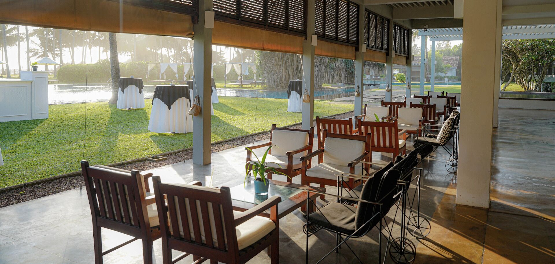 Een overdekt terras met tafels en stoelen, een zwembadje en een gazon.
