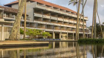 A multi-story hotel with balconies, a swimming pool, and palm trees.