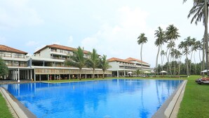 A hotel with a swimming pool, multiple floors, and a covered outdoor area with umbrellas. - The Blue Water - Geoffrey Bawa Heritage Resort Hotel (Wadduwa)
