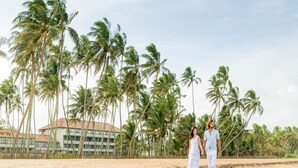 A beach with palm trees and a resort building in the background. - The Blue Water - Geoffrey Bawa Heritage Resort Hotel (Wadduwa)
