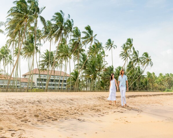A beach with palm trees and a resort building in the background. - The Blue Water - Geoffrey Bawa Heritage Resort Hotel (Wadduwa)