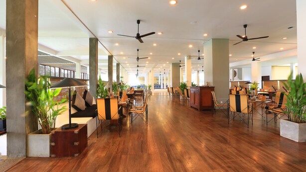 A spacious hotel lobby with wooden flooring, multiple seating areas, ceiling fans, and potted plants. - The Blue Water - Geoffrey Bawa Heritage Resort Hotel (Wadduwa)