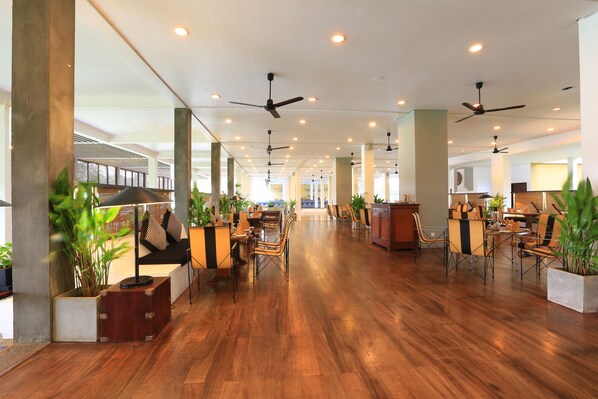 A spacious hotel lobby with wooden flooring, multiple seating areas, ceiling fans, and potted plants. - The Blue Water - Geoffrey Bawa Heritage Resort Hotel (Wadduwa)