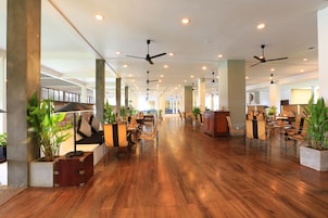 Un amplio vestíbulo de hotel con suelo de madera, varias zonas de estar, ventiladores de techo y plantas en macetas.