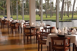 Un restaurante con sillas y mesas de madera, vista a palmeras y un cuerpo de agua al fondo.