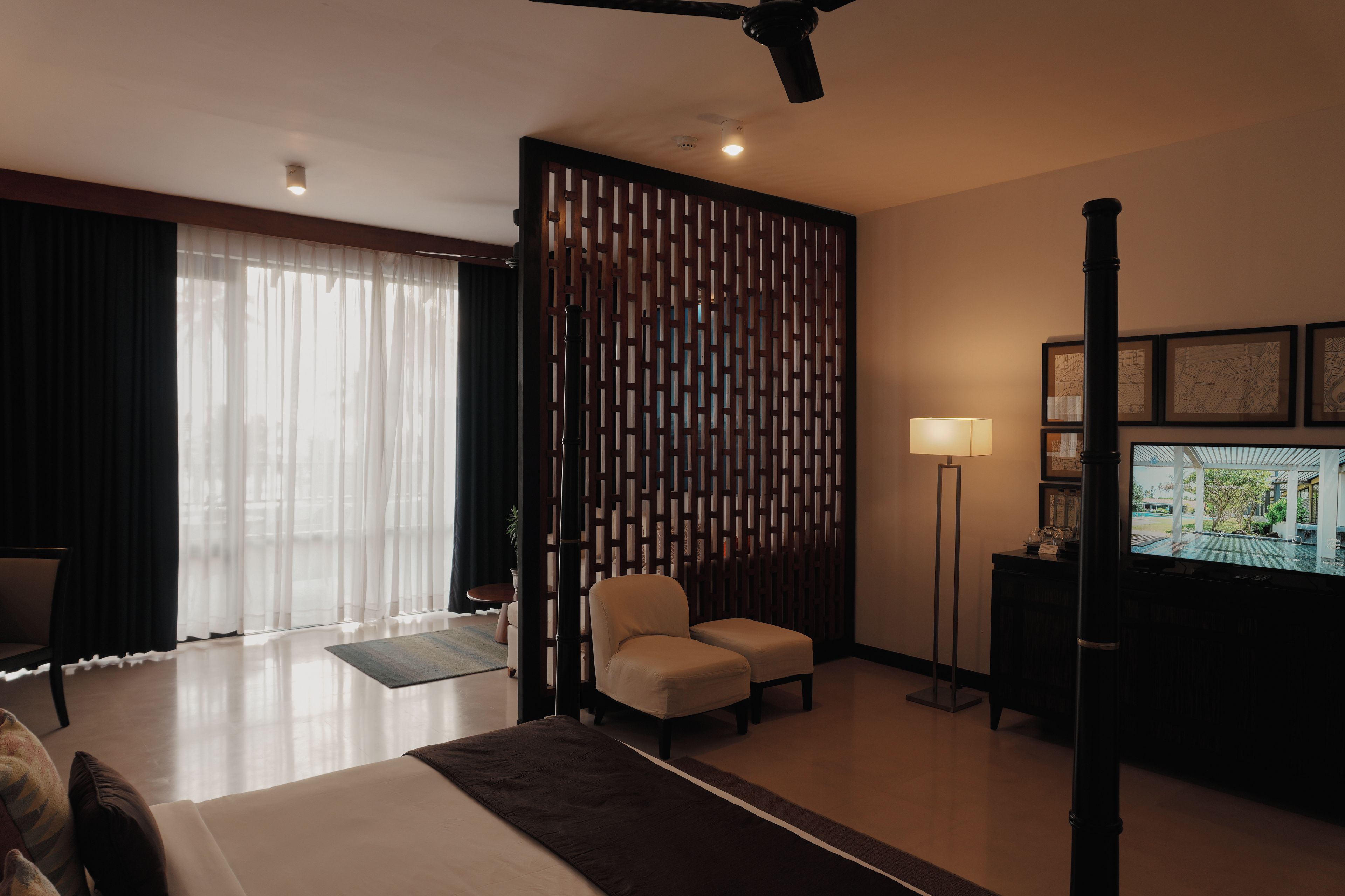 Habitación de hotel con cama, escritorio, silla, televisor y un separador decorativo.