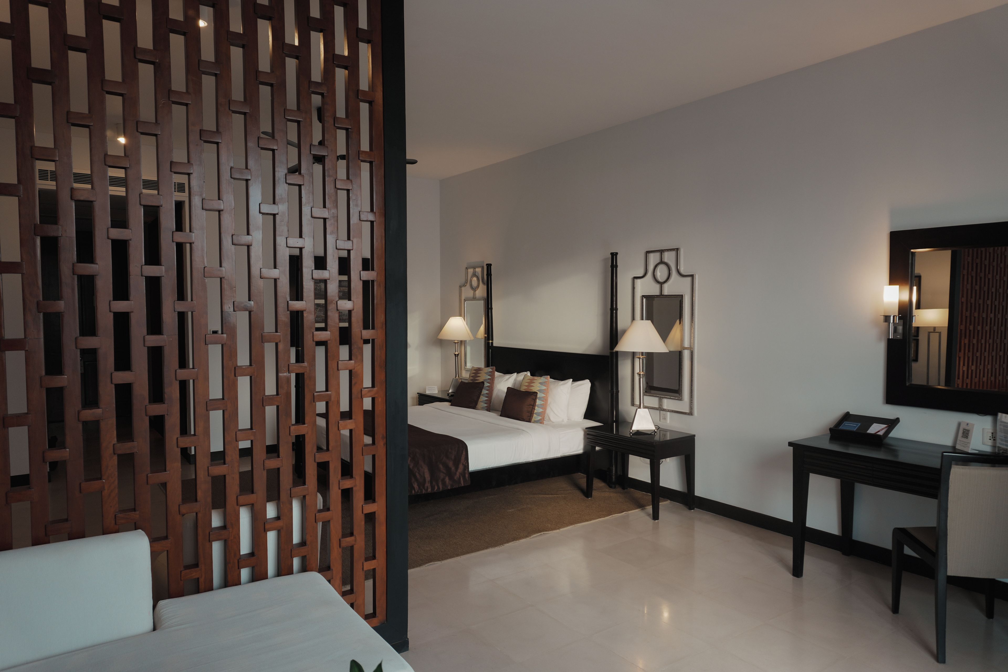 Una habitación de hotel con una cama, mesitas de noche, un escritorio y un espejo.