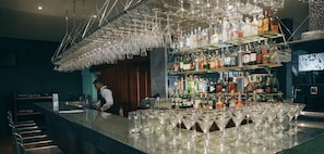 Eine Bar mit einem Barkeeper, Flaschenregalen und zahlreichen hängenden Gläsern.