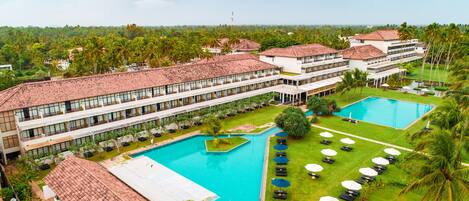 Un resort con varias piscinas, un amplio césped y un edificio de hotel con techo de tejas rojas.