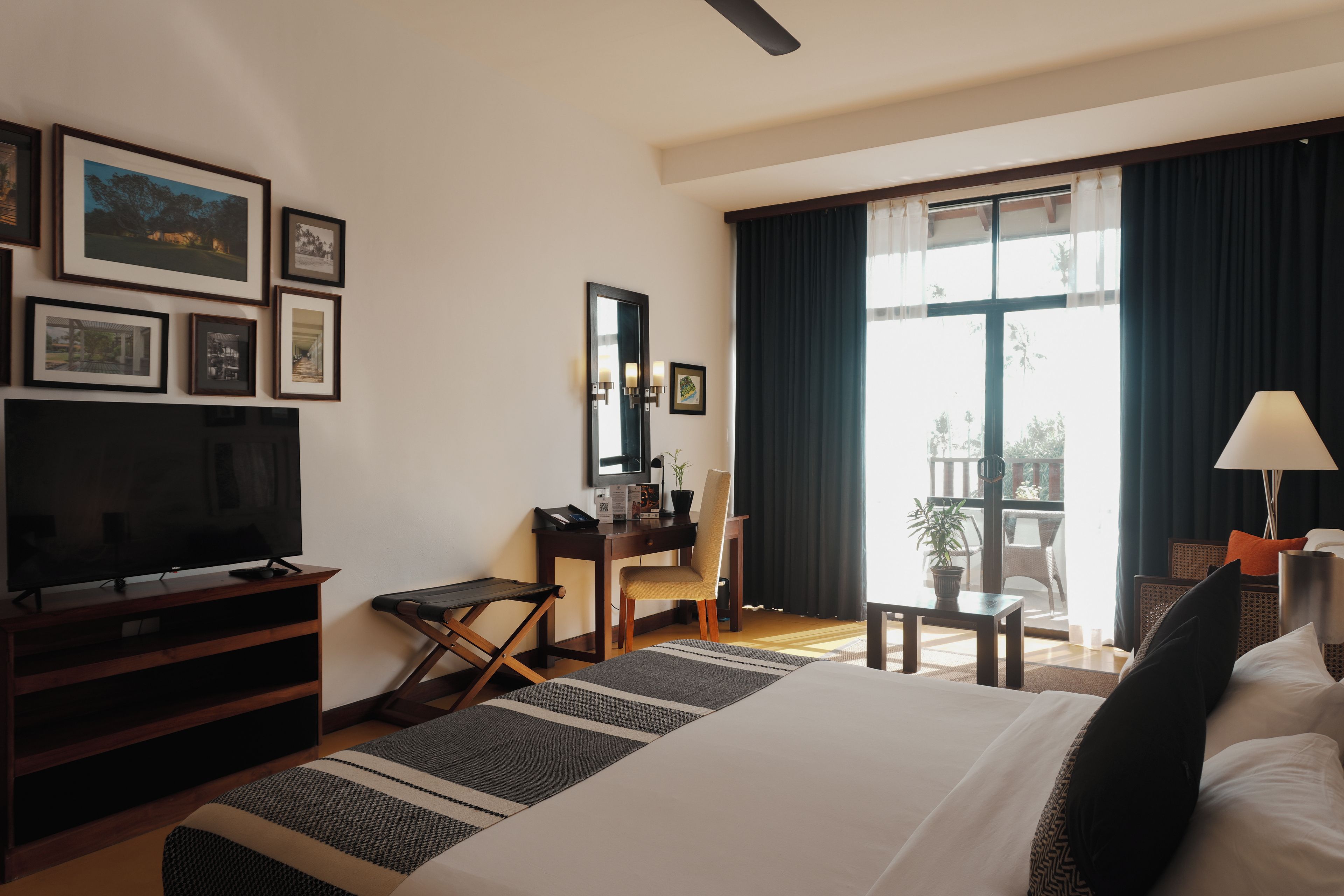 A hotel room with a bed, a desk, a chair, a television, and a balcony with a view.