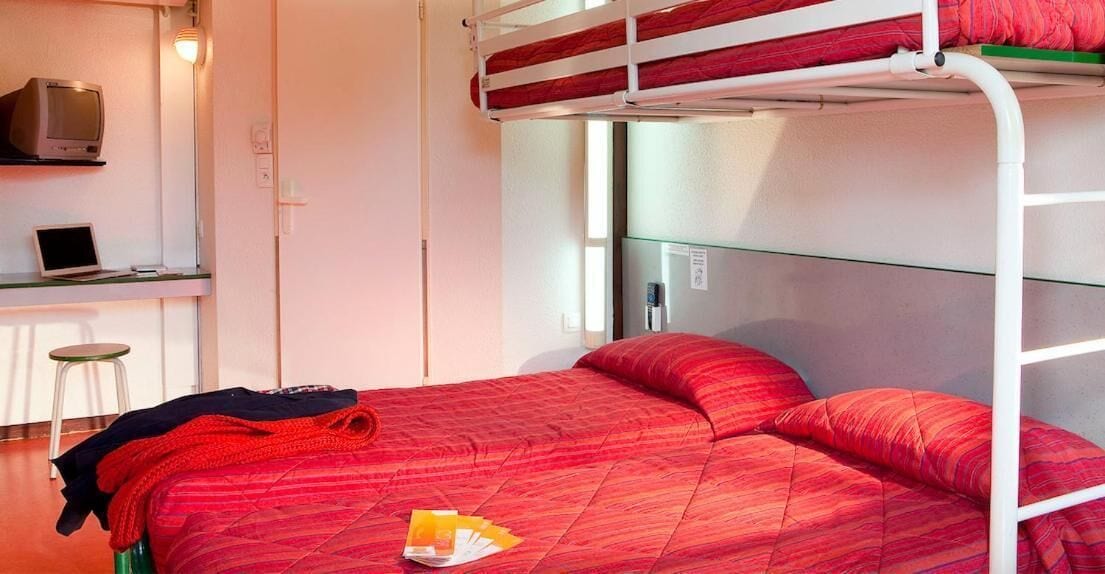 A bunk bed with red bedding, a desk with a laptop, and a chair.